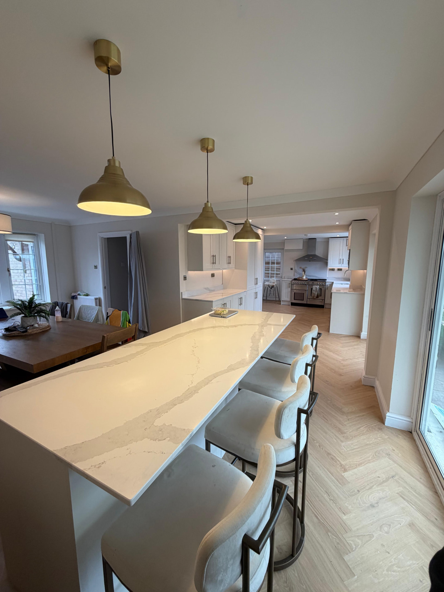 Three brass pendant lights installed over a marble kitchen island in a modern home